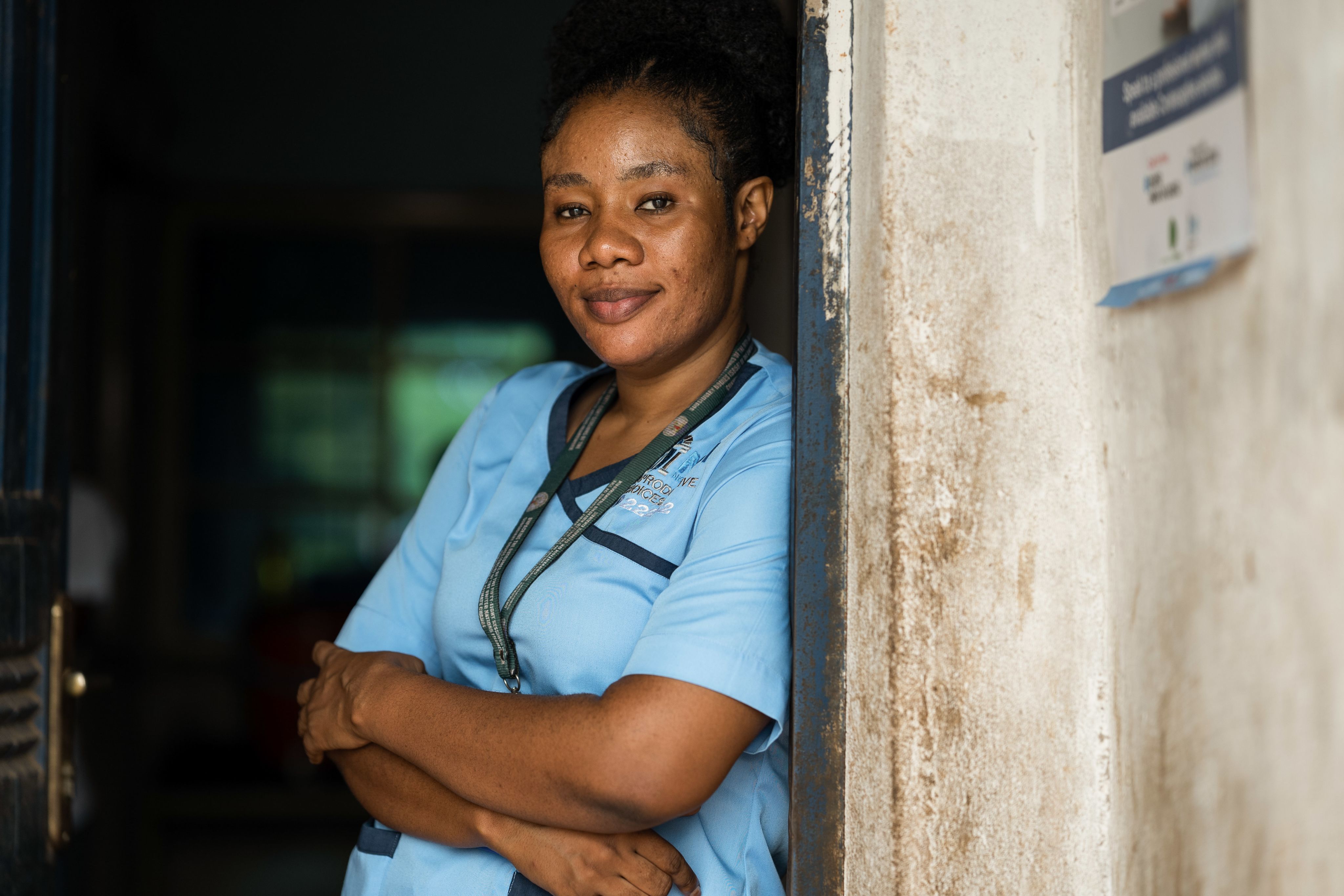 MSI nurse Ify in blue scrubs leaning against a door